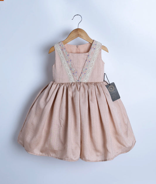 A beige, sleeveless baby frock with embroidered straps and a flared silhouette, displayed on a hanger.