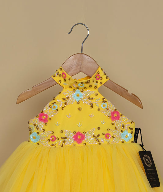 A yellow dress with floral embroidery on a hanger against a beige background.