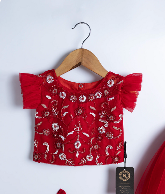 Close view of an red tulle net handworked crop top and skirt is displayed on hangers against a white background.
