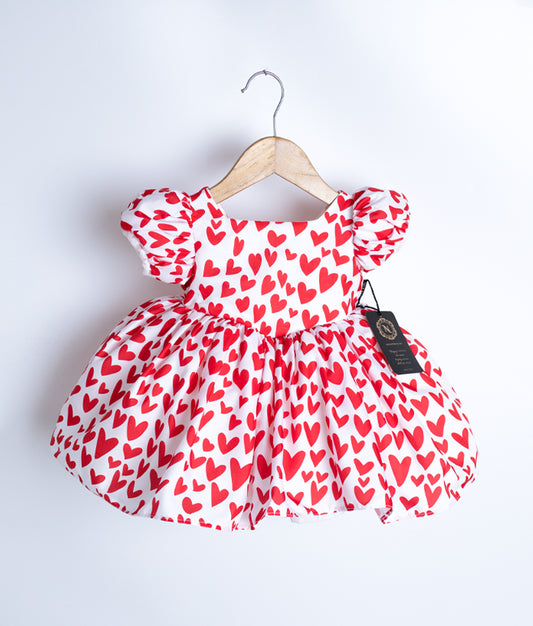 A red and white chiffon baby frock with a heart pattern displayed on a hanger.