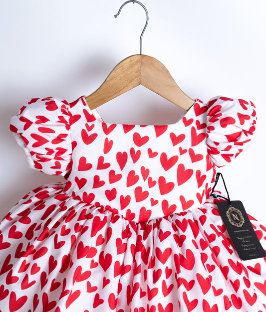 Close view of an red and white chiffon baby frock with a heart pattern displayed on a hanger.
