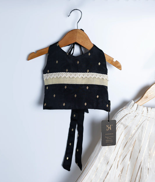 A close view of stylish kidswear set with a black sleeveless embroidered blouse and a white pleated skirt with gold stripes, displayed on wooden hangers.