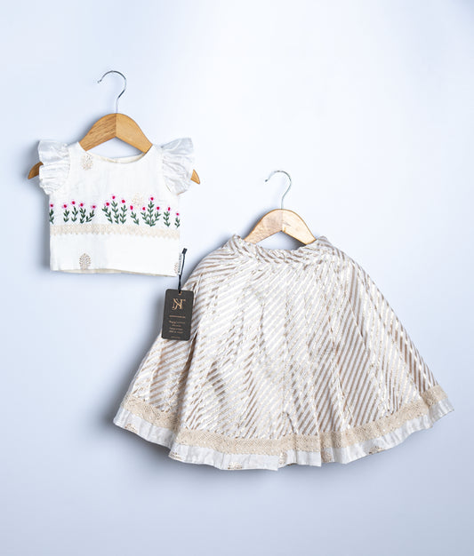 Kids festive outfit with a white crop top featuring pink floral embroidery and frilled sleeves, paired with a cream and gold striped skirt.