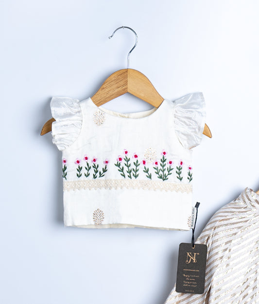 Kids festive outfit with a white crop top featuring pink floral embroidery and frilled sleeves, paired with a cream and gold striped skirt.