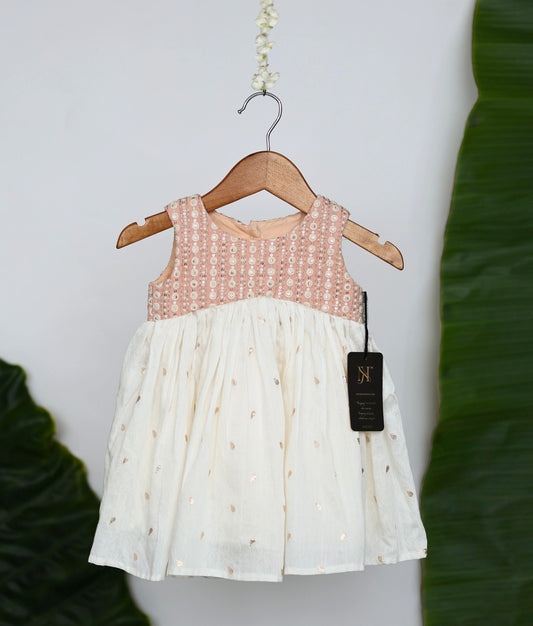 Peach and off-white frock on a wooden hanger against a white background.