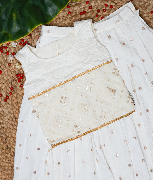 Close view of an elegant white sleeveless ethnic dress for kids featuring intricate golden embroidery on the yoke and a pleated skirt with subtle sequin detailing—ideal for festive occasions.