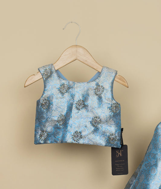 Sky blue handworked floral-patterned top on a hanger against a beige background.