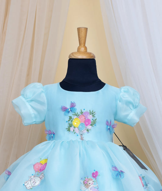 Close view of an sky blue dress with baloon theme on a mannequin against a beige curtain background.