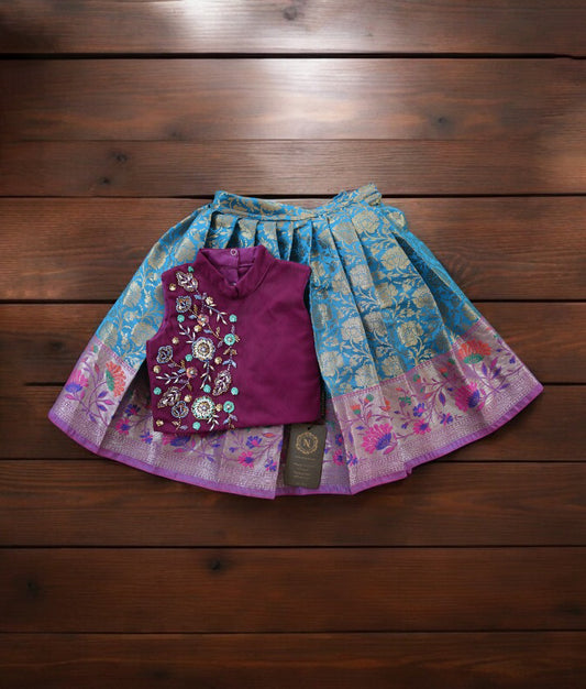A grape wine and blue handworked crop top paired with a Banarasi skirt, displayed on a wooden surface.