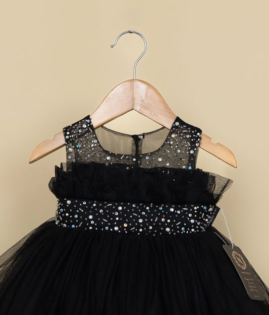 Close view of a black tulle net dress with sequin details on a hanger against a beige background.