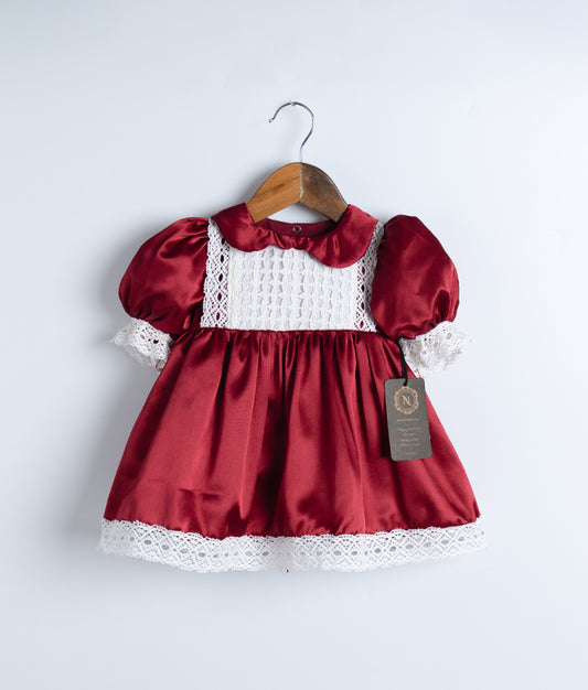 A maroon christmas frock with lace detailing and puff sleeves, displayed on a wooden hanger.