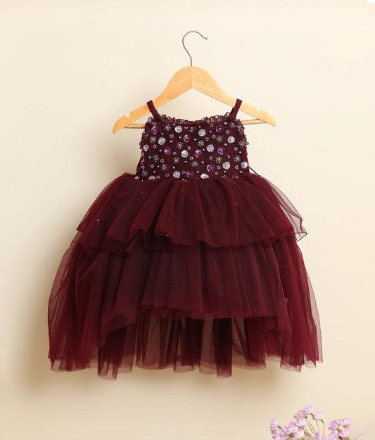 Front view of a wine-red tulle net handworked high-low birthday frock against plain background