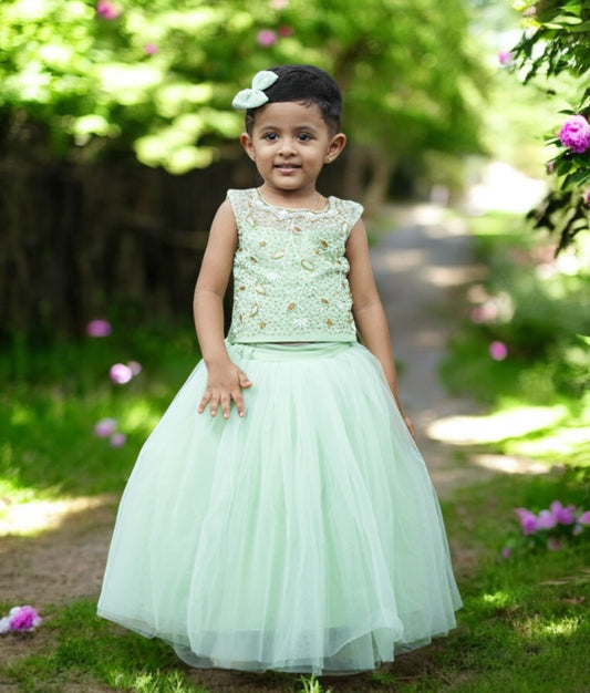 A baby girl wearing a pastel green hand-worked crop top with a full skirt, posing outdoors.