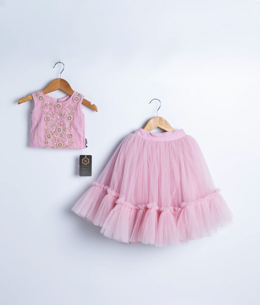 A pink crop top with handwork and a full-length pink skirt displayed on wooden hangers against a white background.