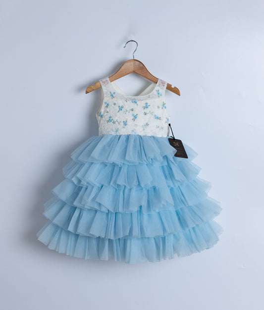 An off-white embroidery yoke with a blue skirt birthday frock for a baby girl, displayed on a wooden hanger.