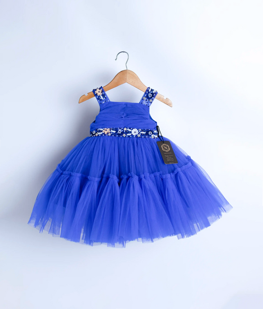 A blue tulle net handwork birthday frock displayed on a hanger.