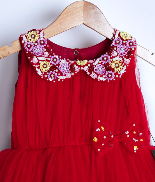 Close view of an red tulle net frock displayed on a wooden hanger.