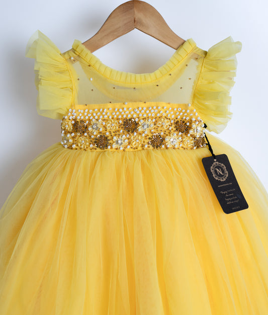 Close view of an yellow tulle net frock displayed on the hanger.