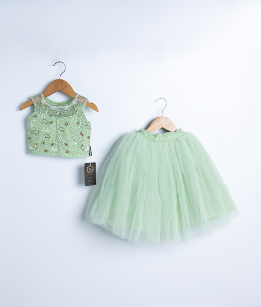 A pastel green crop top and a skirt displayed on a wooden hangers.