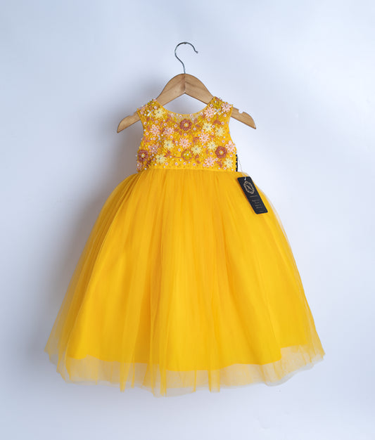 A mango yellow tulle net frock with handworked flower designs on the bodice, displayed on a hanger.