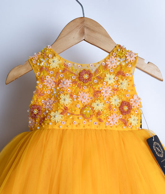 Close view of an mango yellow tulle net frock with handworked flower designs on the bodice, displayed on a hanger.