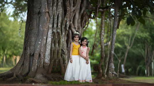 Two girls wearing Diwali dresses standing under a big tree.