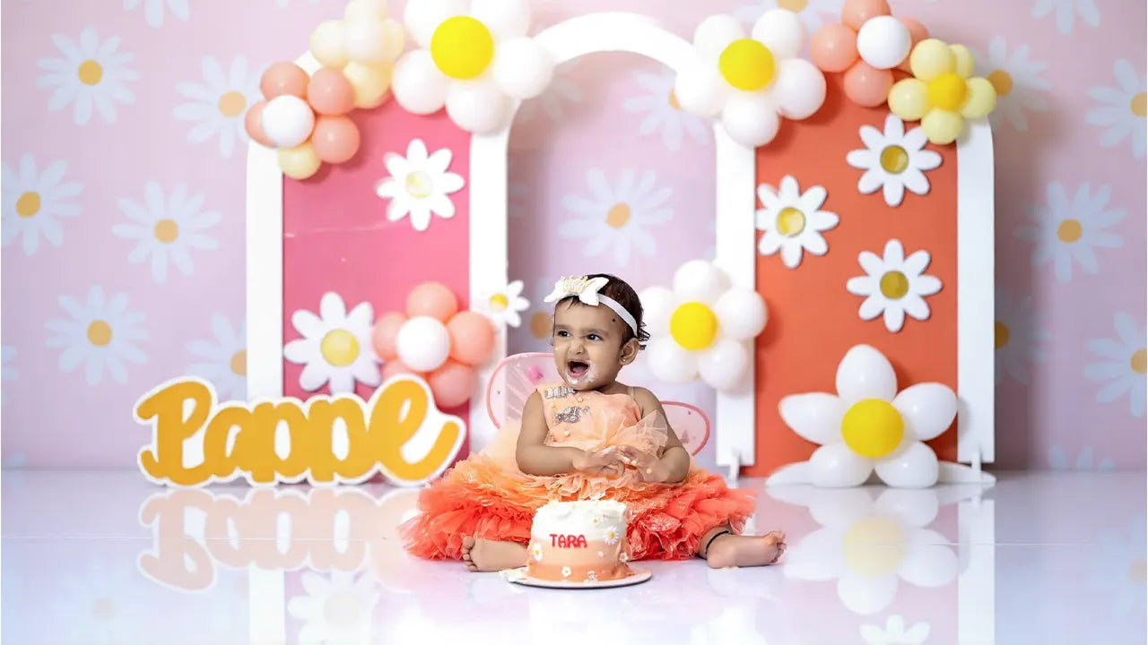 A baby girl celebrating her first birthday in a peach luxury frock with a cake smash theme.