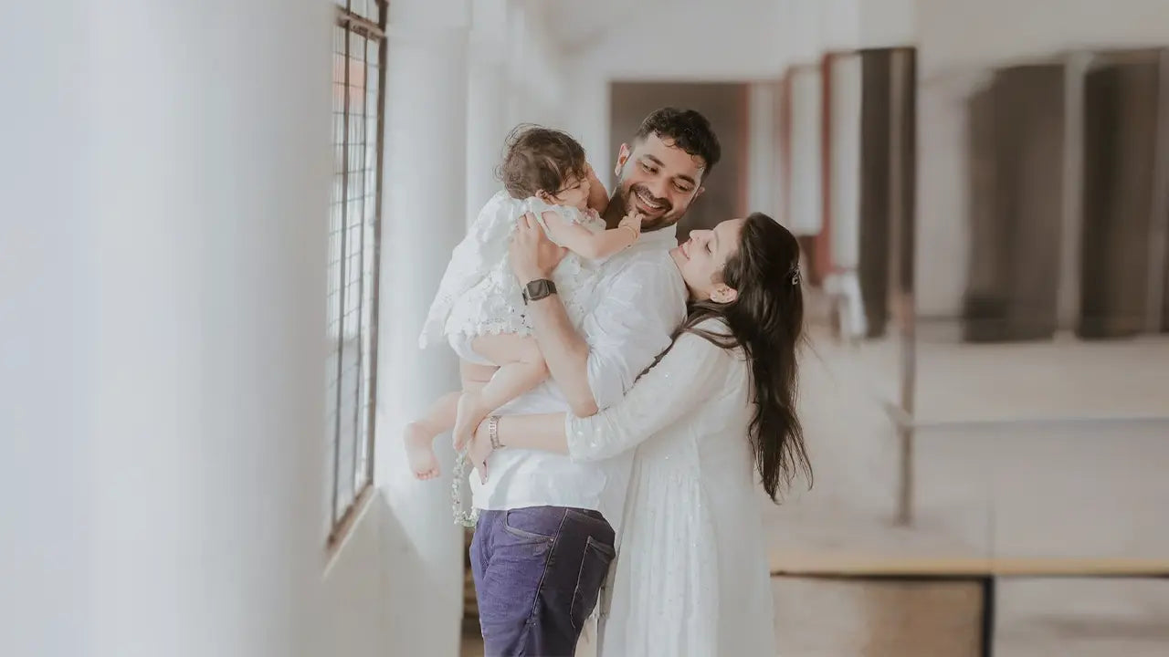 A happy family in Kerala celebrating a ceremony with their baby wearing a white baptism dress.