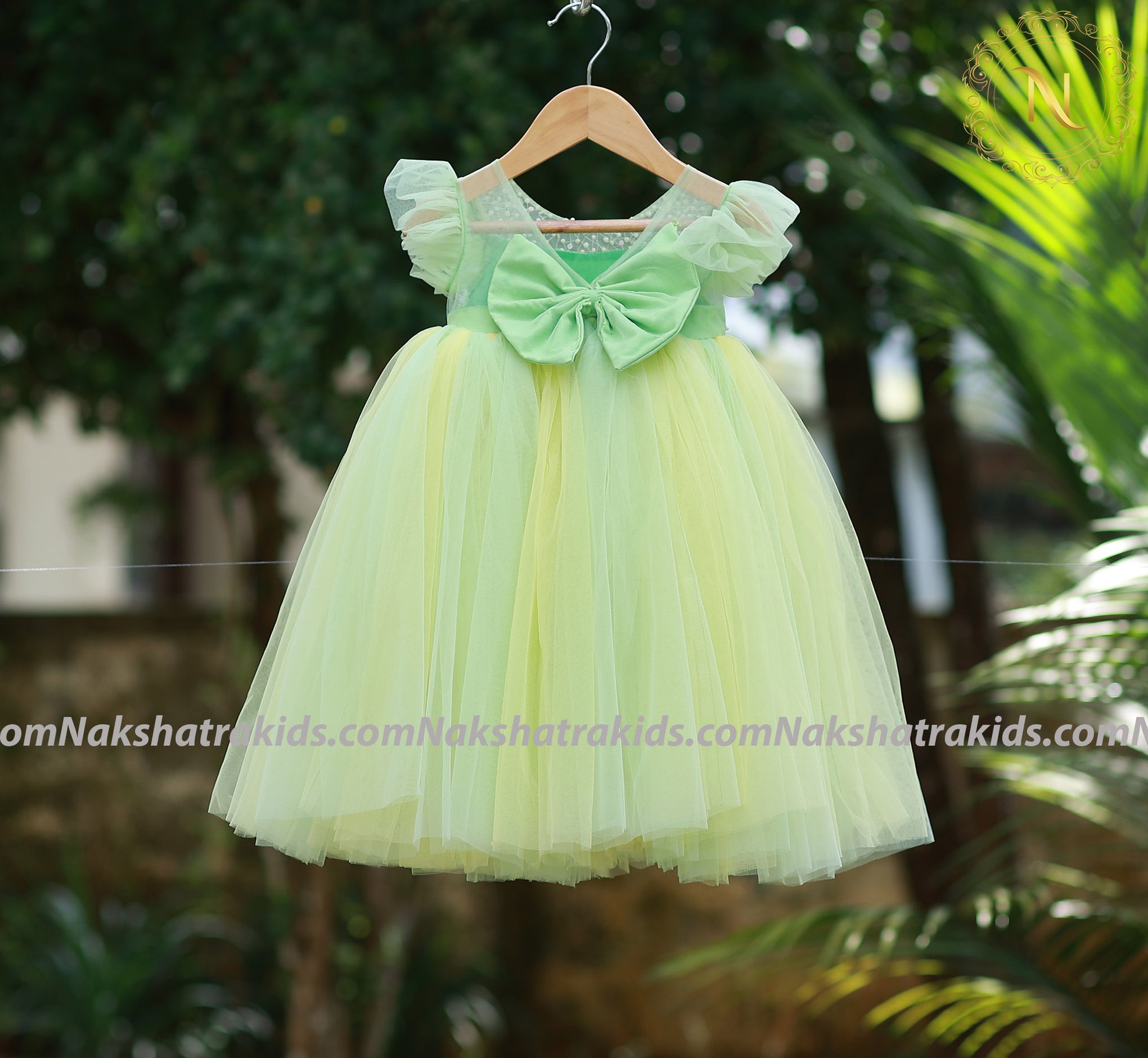 Back view of a green and yellow dress on a hanger against a nature background.