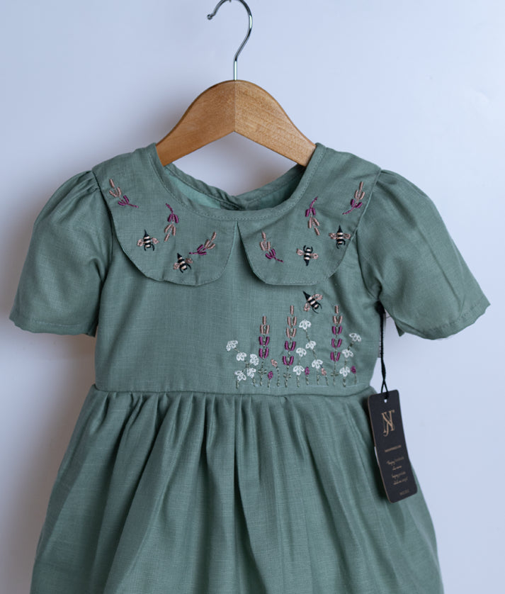 Close view of an pastel green cotton frock displayed on a hanger.