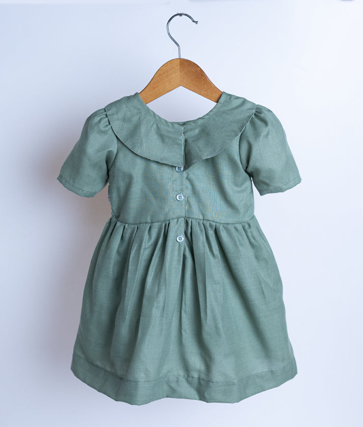 Back view of an pastel green cotton frock displayed on a hanger.