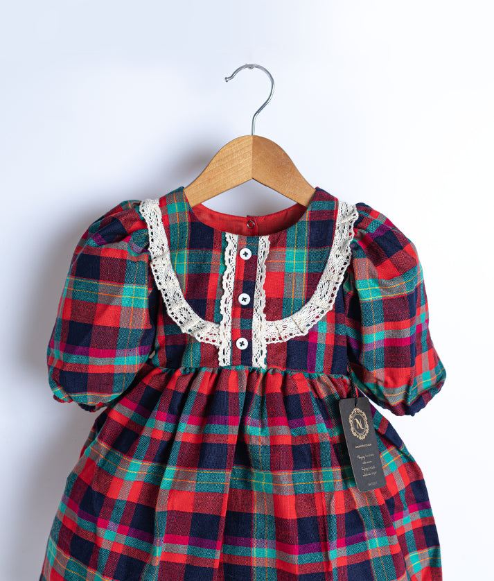 Close view of an red cotton checked christmas frock displayed on a hanger. 