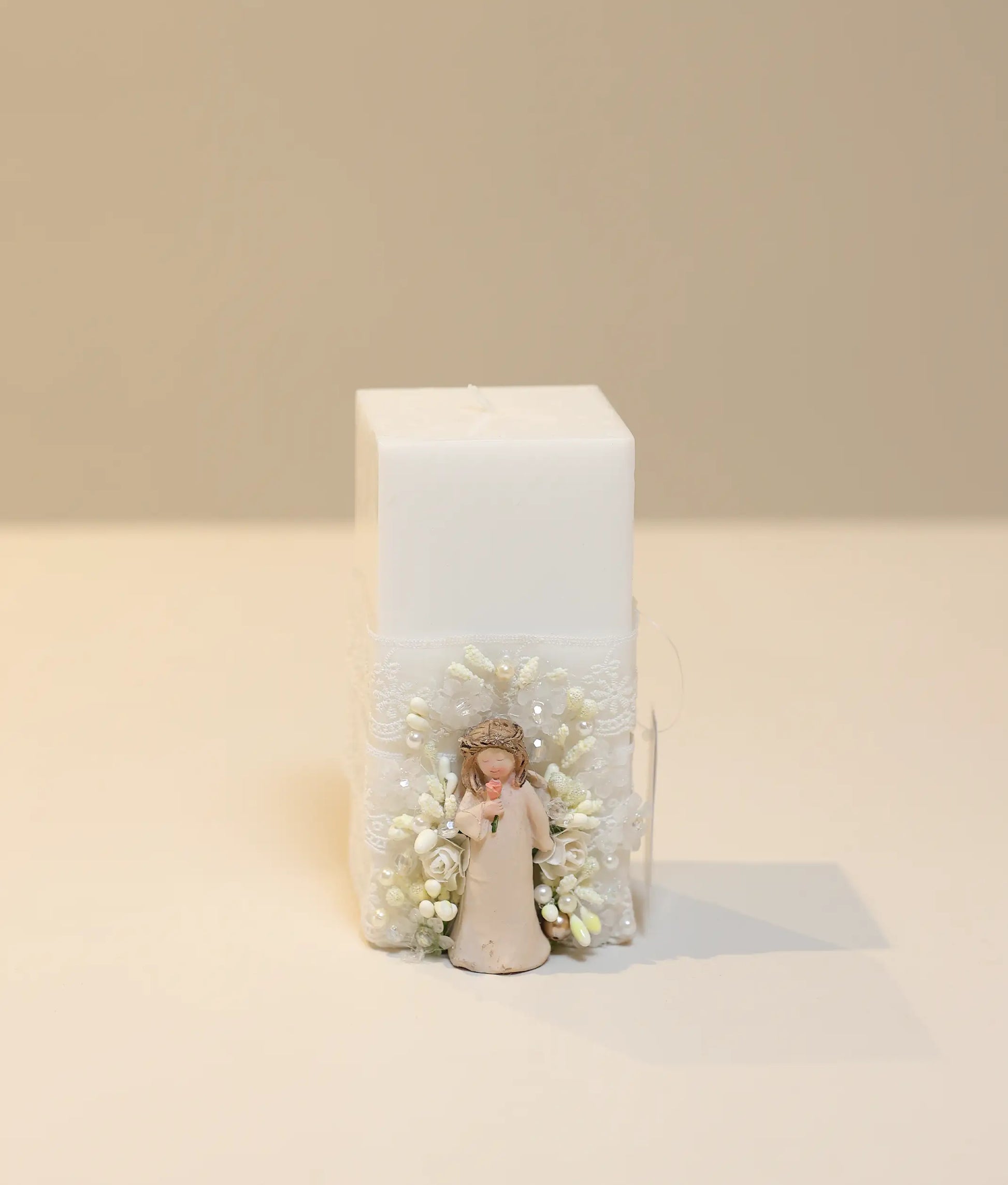 Decorative pillar candle for baby baptism featuring an angel charm, gold pearls, and white lace ruffles
