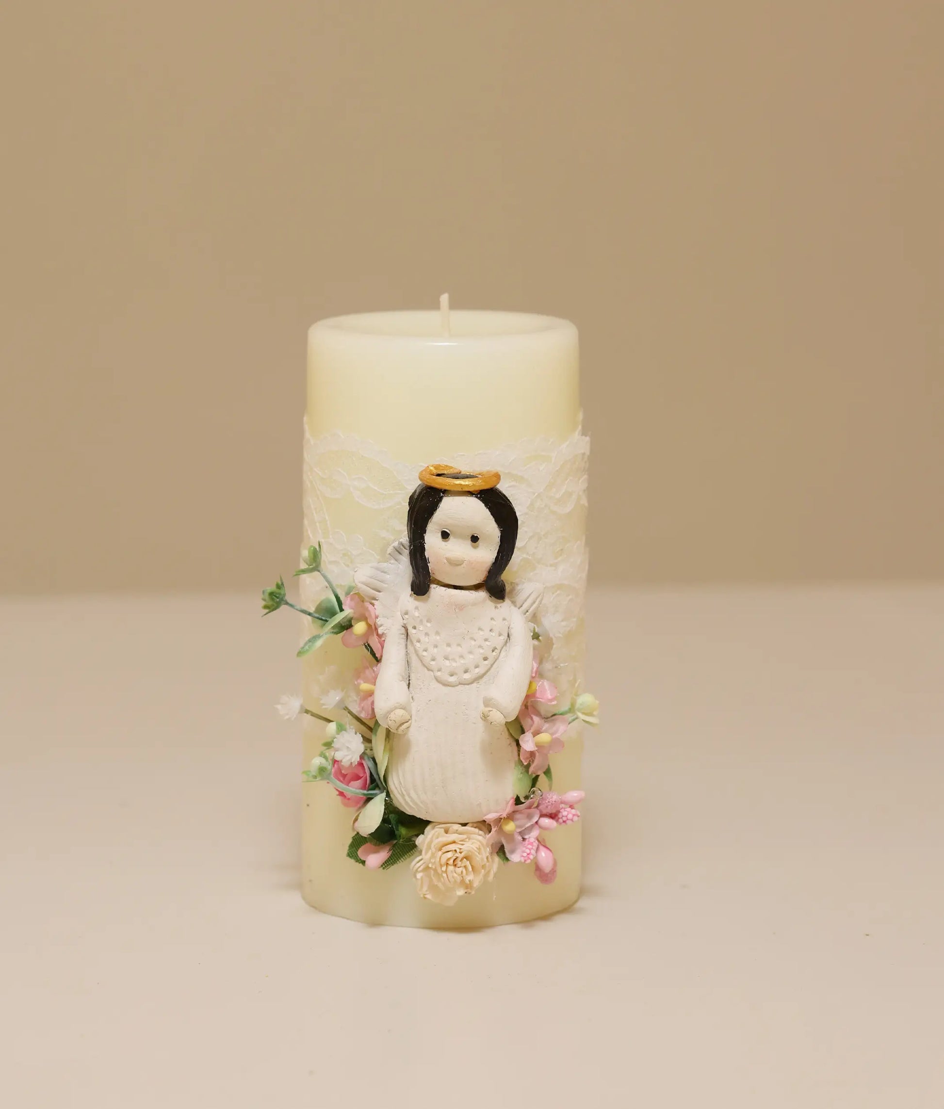 White decorative baptism candle featuring a miniature angel figurine, silk flowers, and delicate lace ruffles