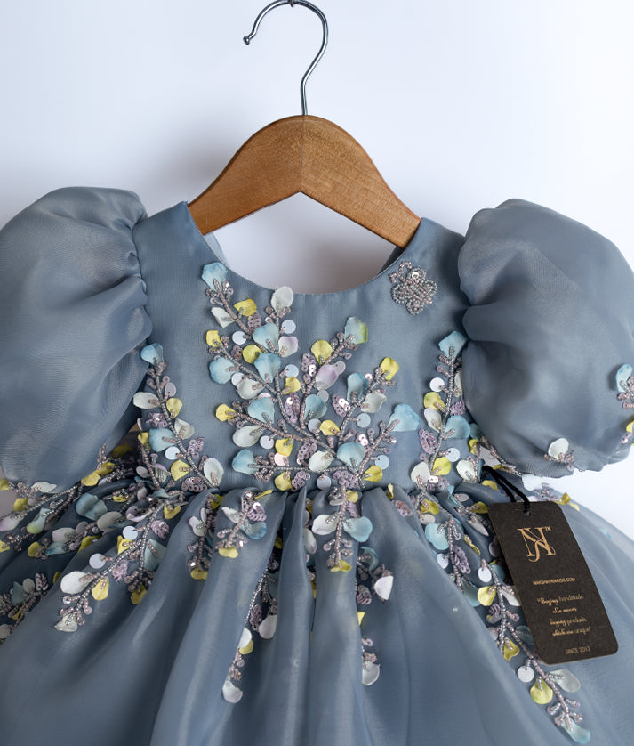 Close-up of the ash dress bodice showing the intricate pastel floral handwork and butterfly detail on the shoulder