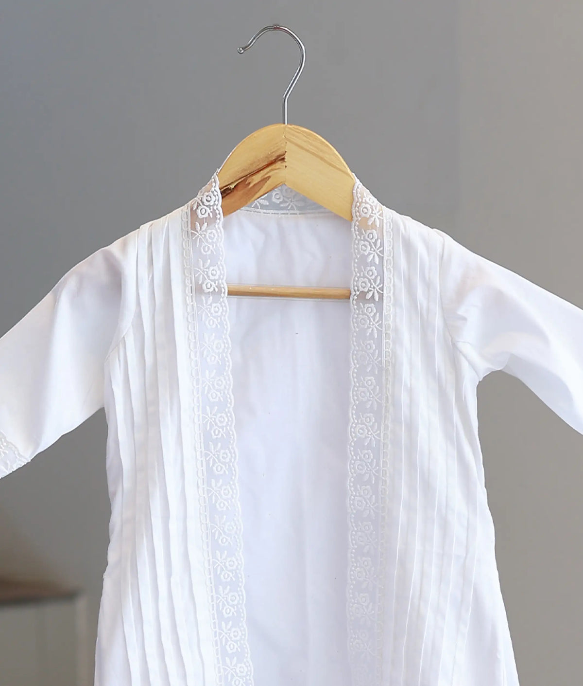 Close-up detail of baby baptism gown open front placket showcasing fine vertical pin-tucks and intricate floral lace border trim.