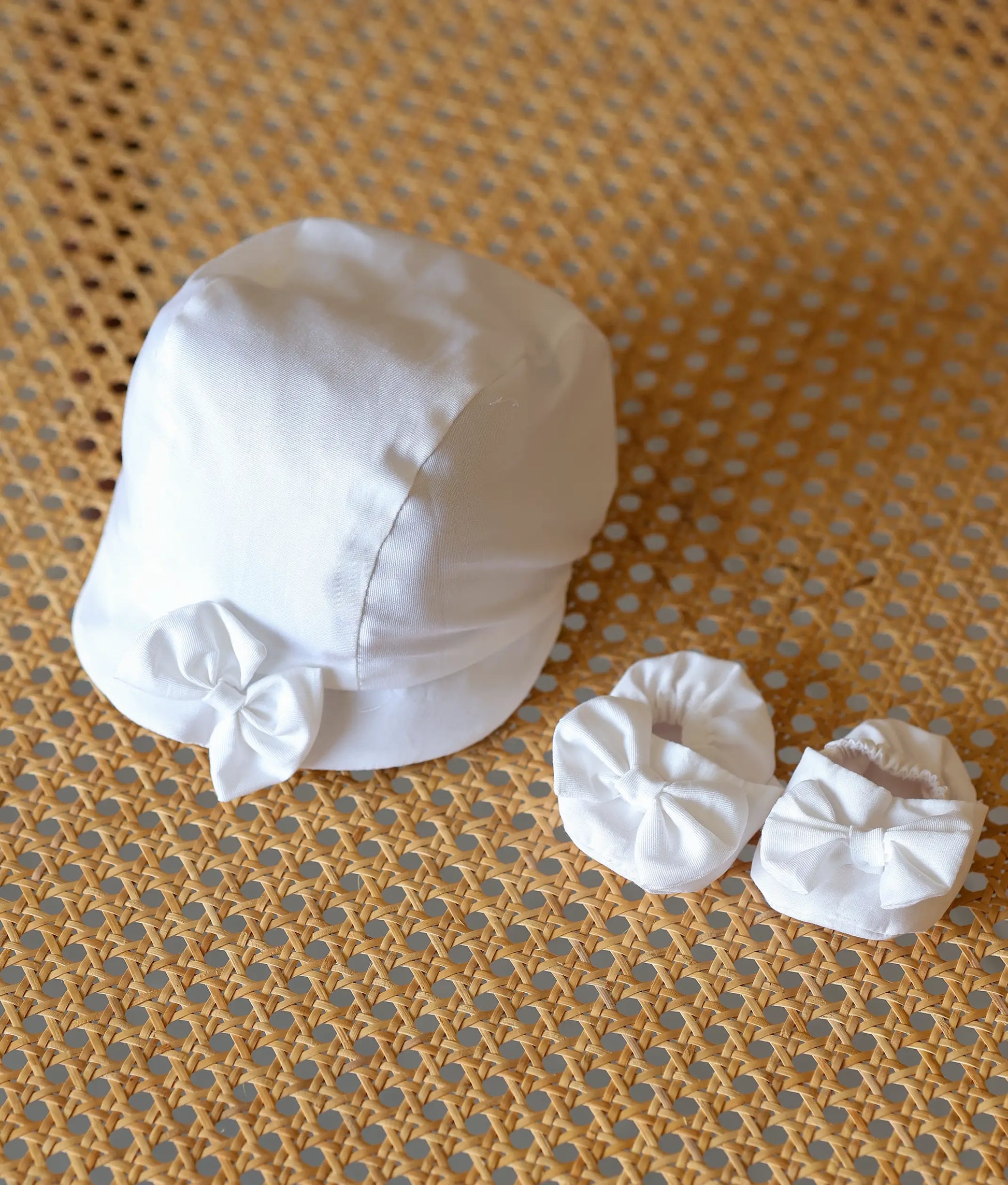 A matching white baby boy baptism cap and soft booties decorated with small white bows.