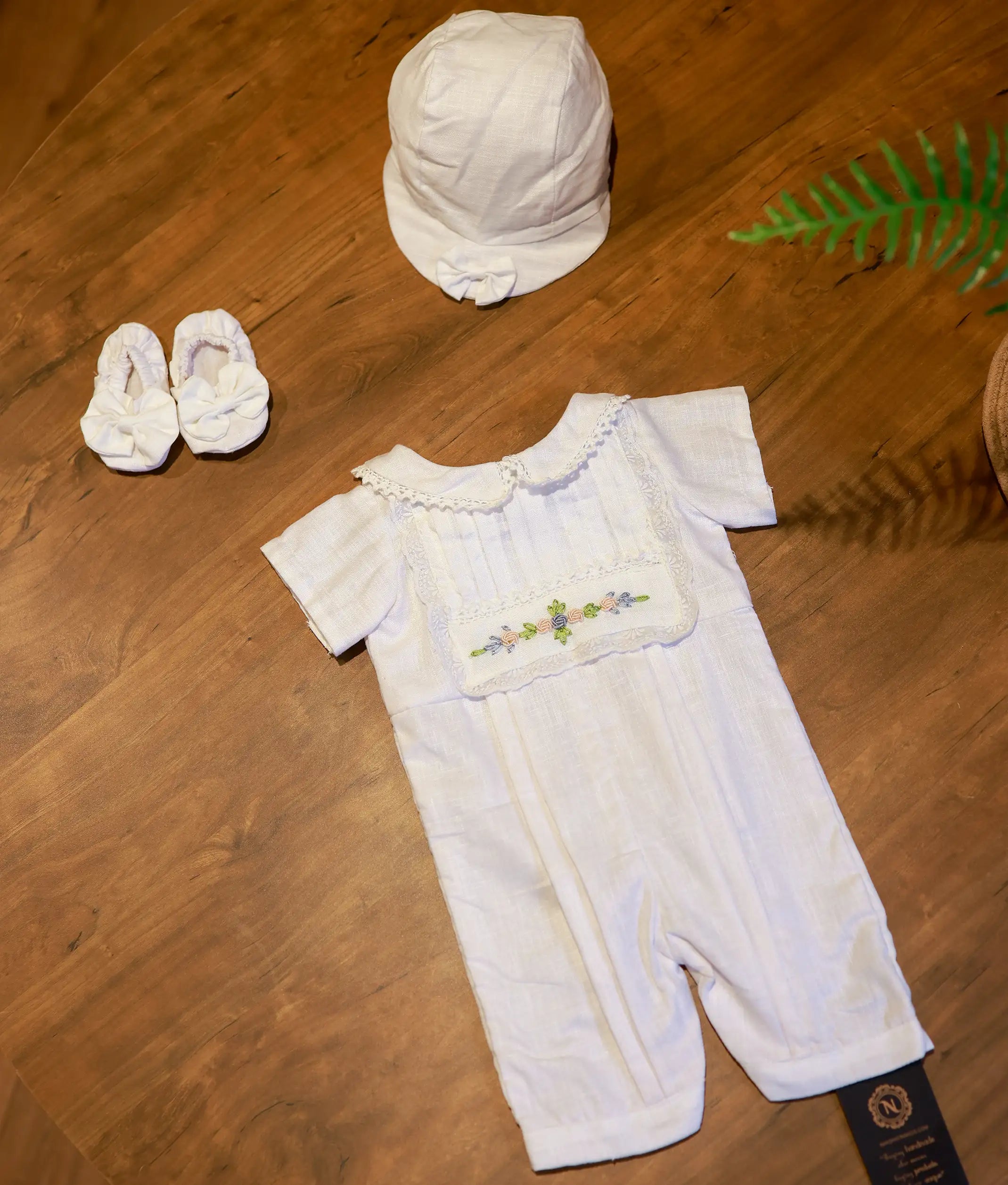 A complete three piece baptism set for baby boys including the hand-embroidered romper, a matching white cap with a bow, and fabric booties