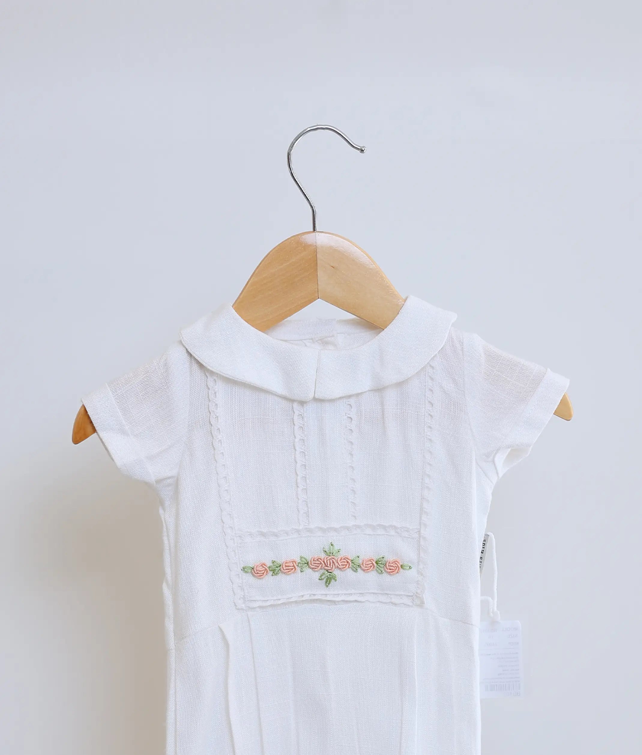 Close-up of pink and green floral hand-embroidery on a white cotton baby boy christening romper with a Peter Pan collar.