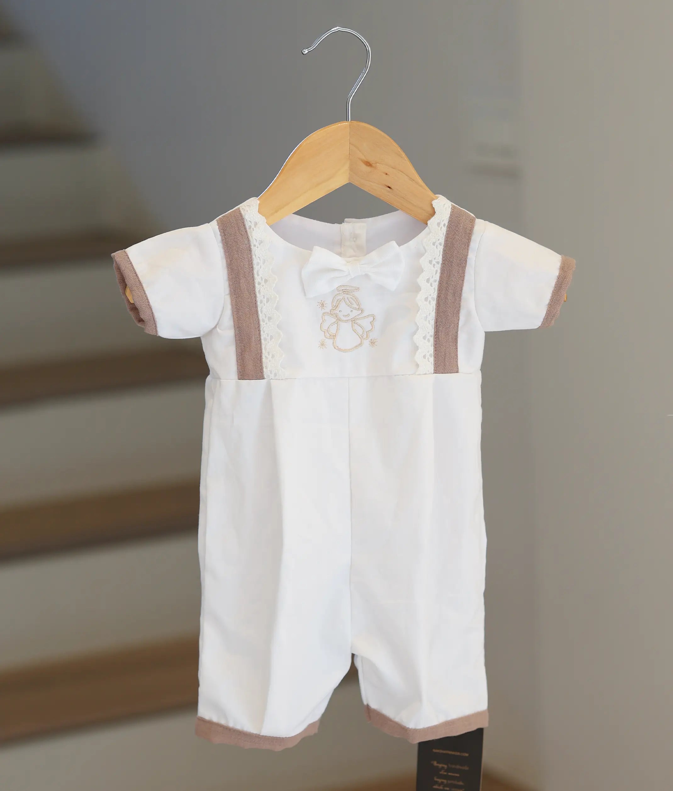 Front view of a white baby boy baptism romper with angel embroidery and beige accents.