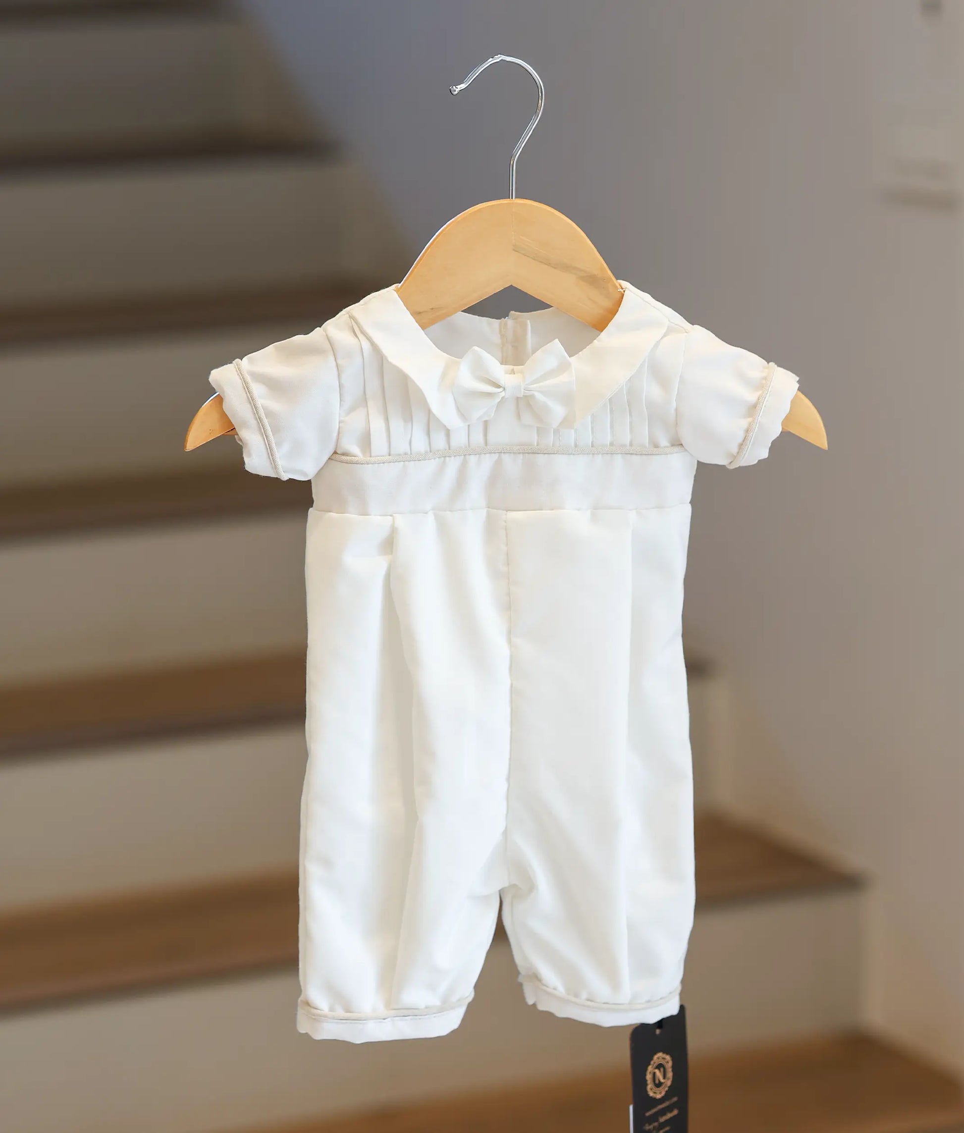 Full front view of a baby boy's white baptism romper with cream borders.