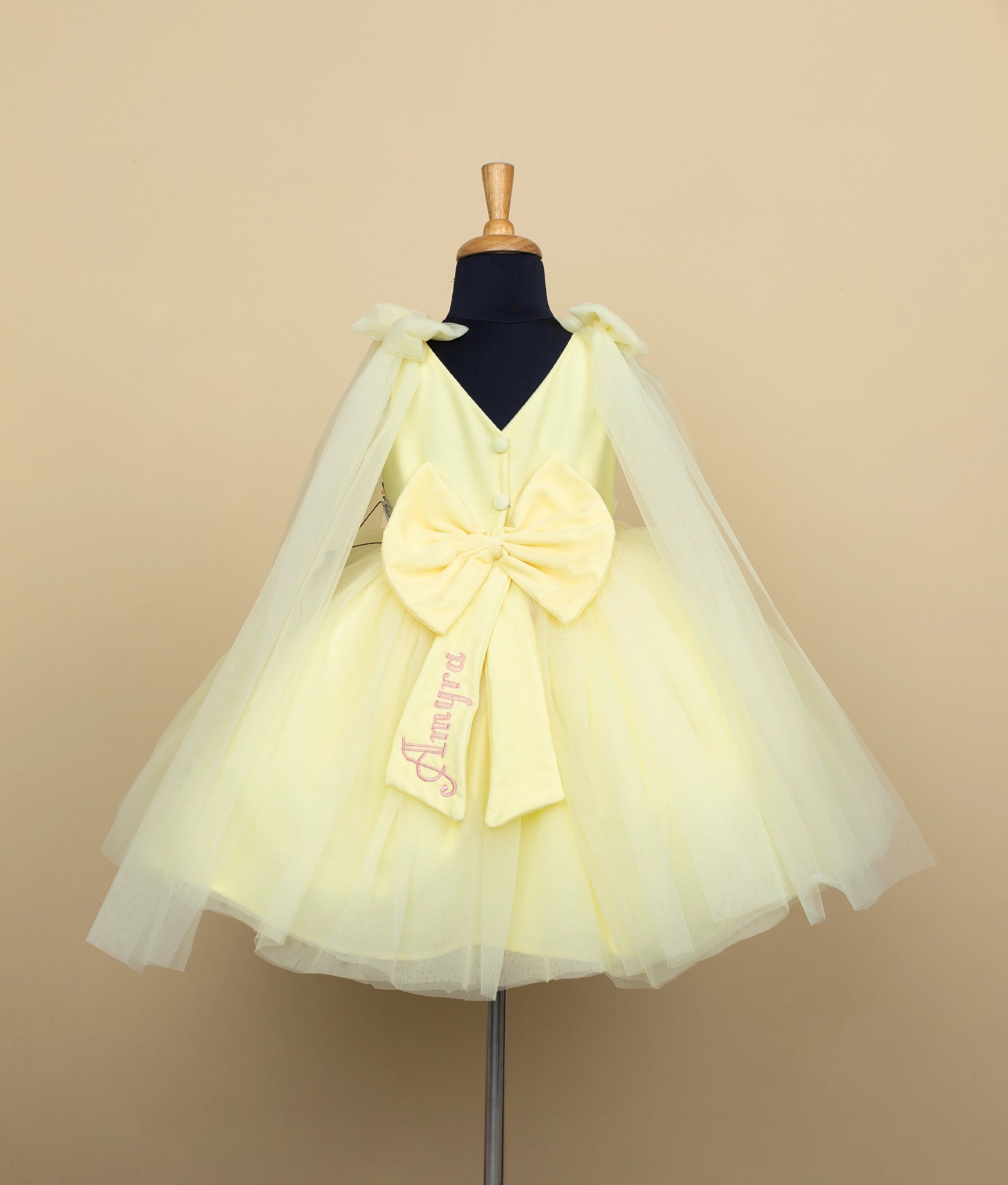Side angle view of baby formal dress in cream with yellow floral details and layered tulle bottom
