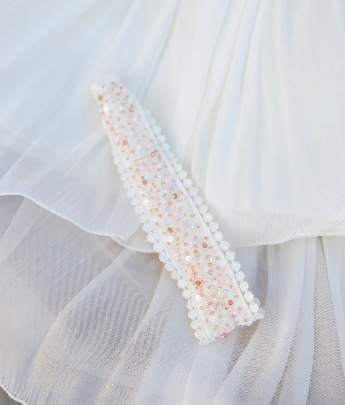 Detailed view of hand-beaded off-white headband with delicate lace edging laid on the baptism gown.