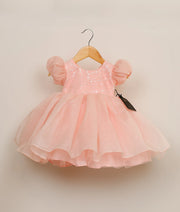 Front view of a pastel pink crush organza birthday frock for baby girls featuring a sequin-embellished yoke and a multi-layered voluminous skirt