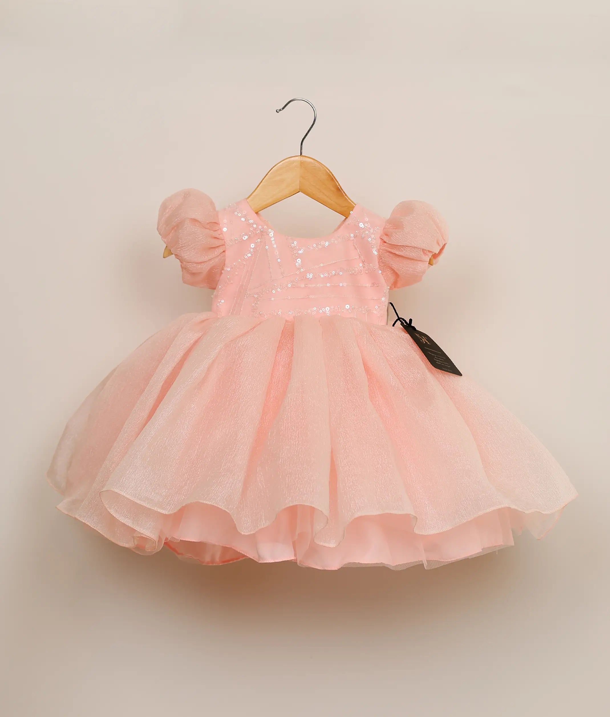 Front view of a pastel pink crush organza birthday frock for baby girls featuring a sequin-embellished yoke and a multi-layered voluminous skirt