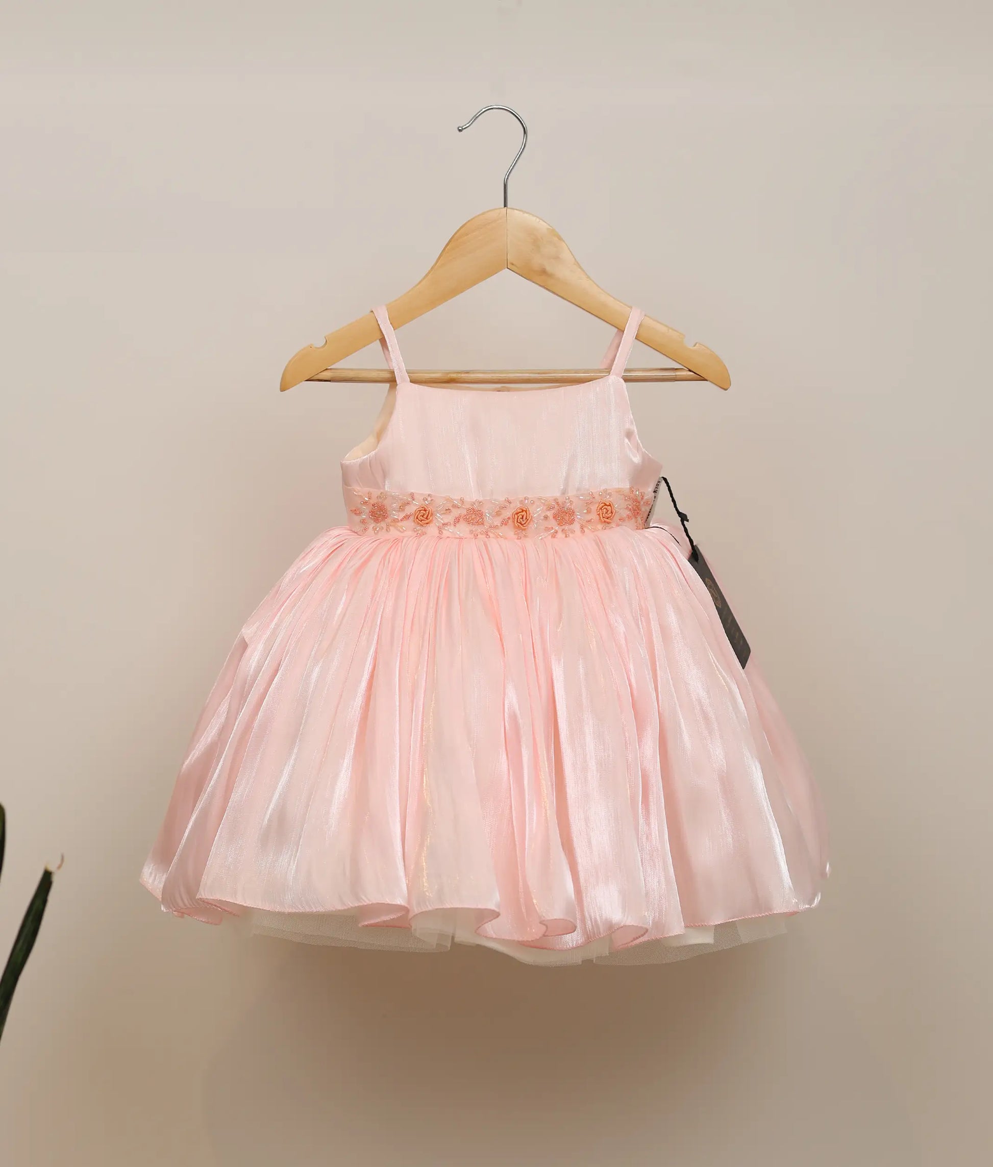Front view of a pastel pink laser organza handworked birthday frock for baby girls featuring spaghetti straps and a voluminous flared skirt