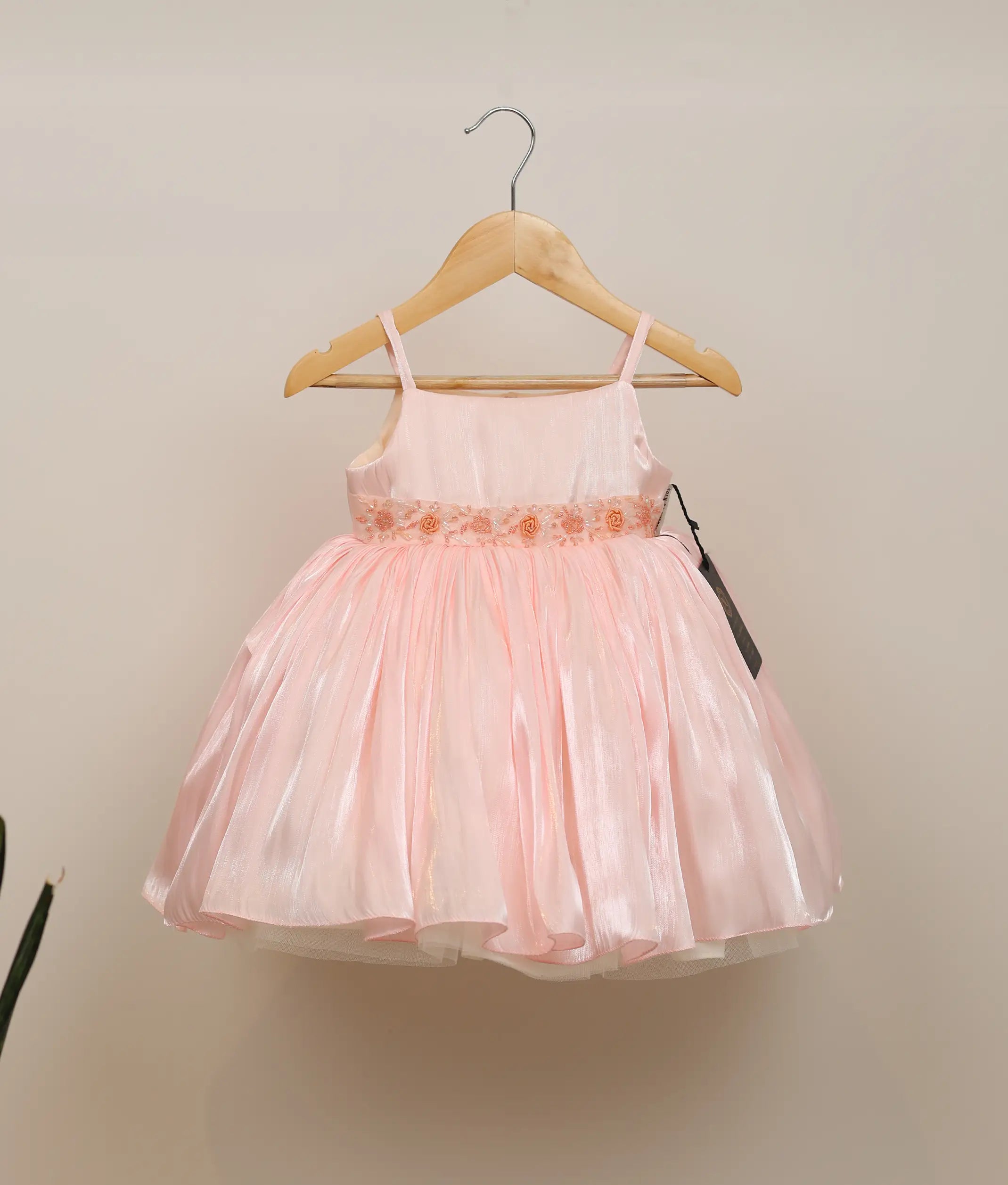 Front view of a pastel pink laser organza handworked birthday frock for baby girls featuring spaghetti straps and a voluminous flared skirt
