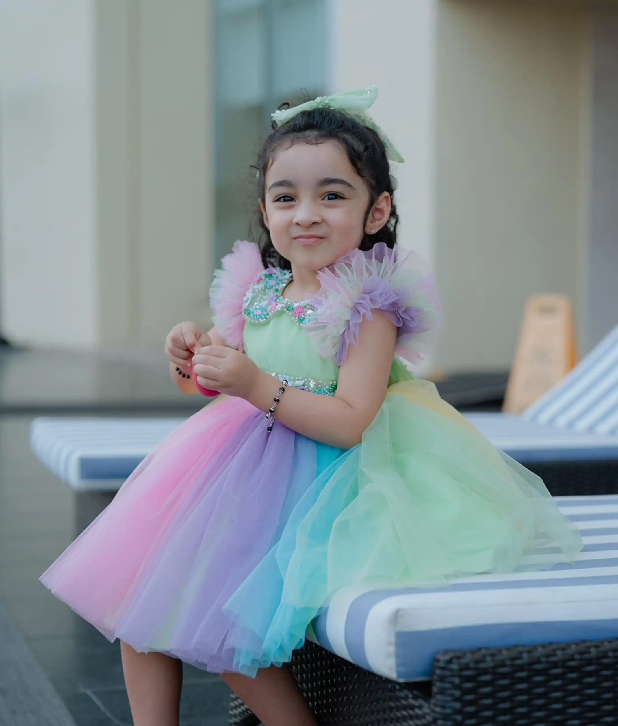 A baby girl wearing a multicolored rainbow-themed birthday frock with a Peter Pan collar and butterfly sleeves