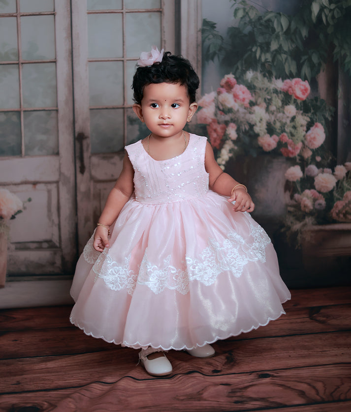 Baby girl wearing a peach shimmer organza birthday frock with a voluminous scalloped skirt and lace detailing