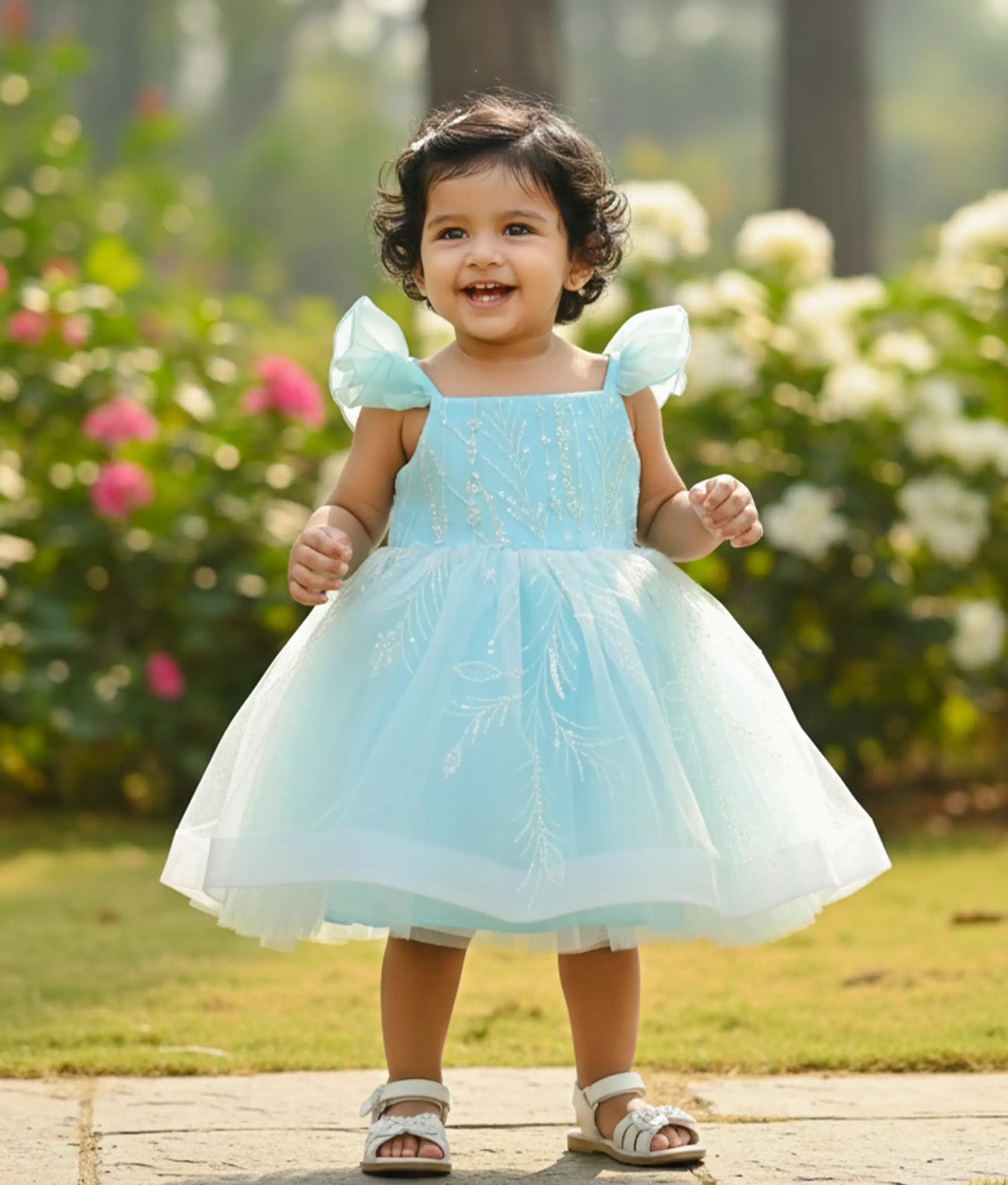 Baby girl wearing a sky blue tulle net birthday frock for baby girls featuring floral vine work material and butterfly sleeves